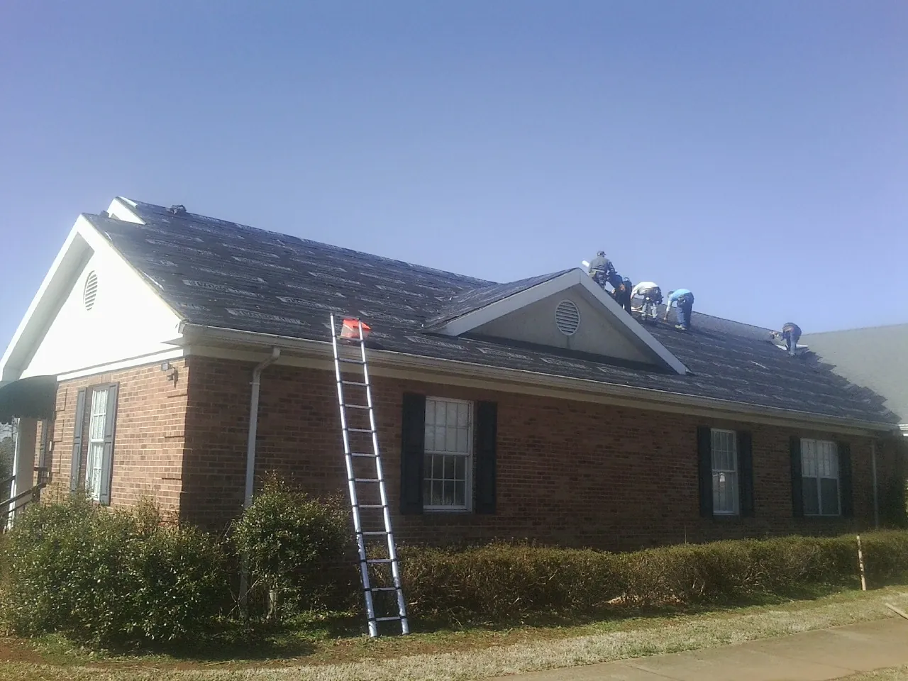 Crew tearing shingles off a brick ranch roof with a ladder set — Emergency Roof Repair work by our crew in Hudson